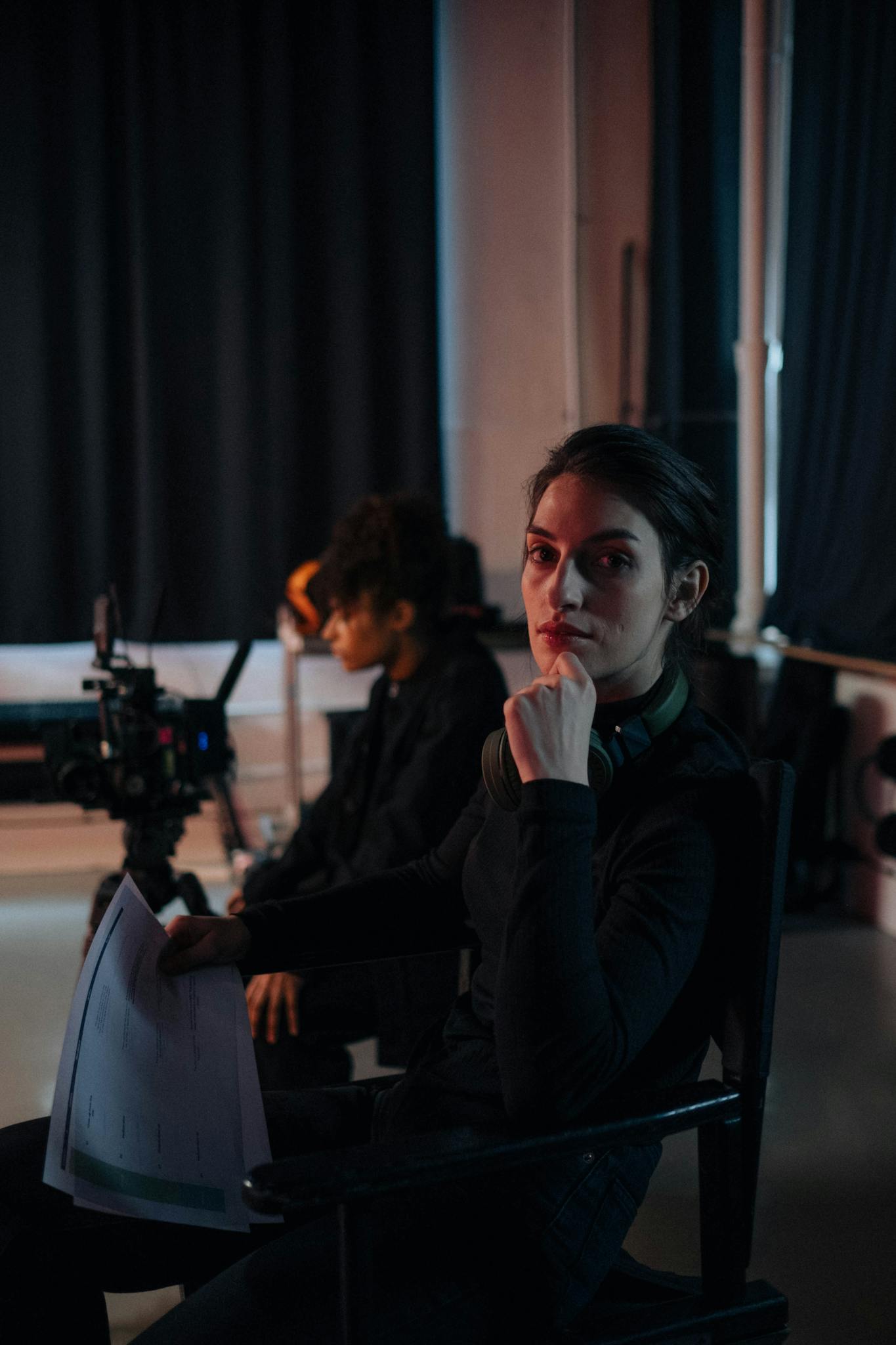 A focused female director sits holding a script on a film set, emphasizing creativity and teamwork.