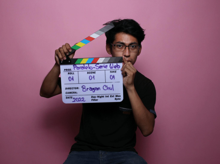 Portrait of an adult male holding a clapperboard in front of a pink background during a studio shoot.